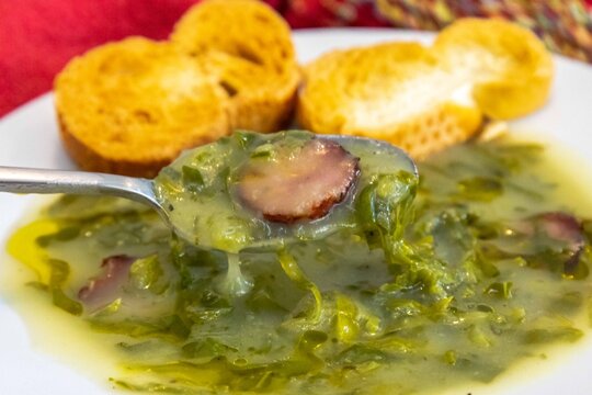 Traditional Portuguese caldo verde soup with chouri&ccedil;o sausage, olive oil and toasted bread, top view