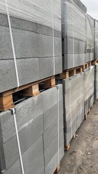 Stacked and wrapped conPallets of grey concrete hollow masonry blocks wrapped and strapped in storage.crete block pallets in outdoor storage.