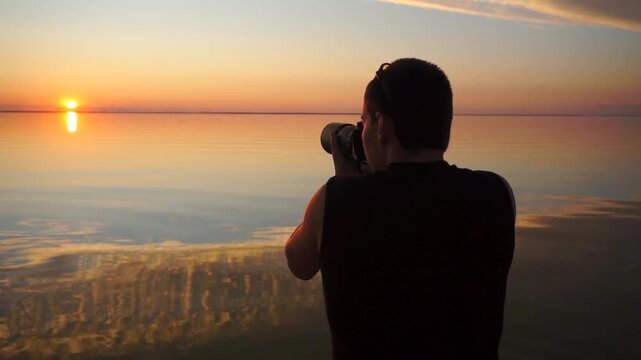 Back view of male professional photographer with camera and tripod taking photos calm sea sunset