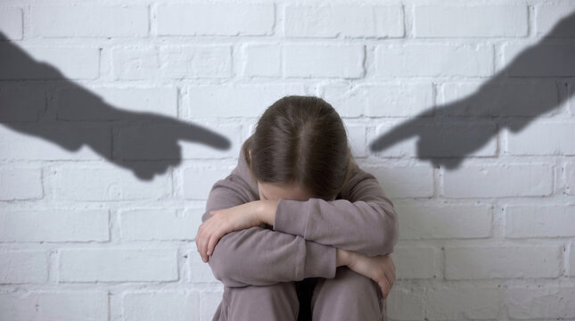 Sad Young Girl Sitting on Floor While Dark Shadows Point Accusingly at Her, Conceptual Representation of Bullying