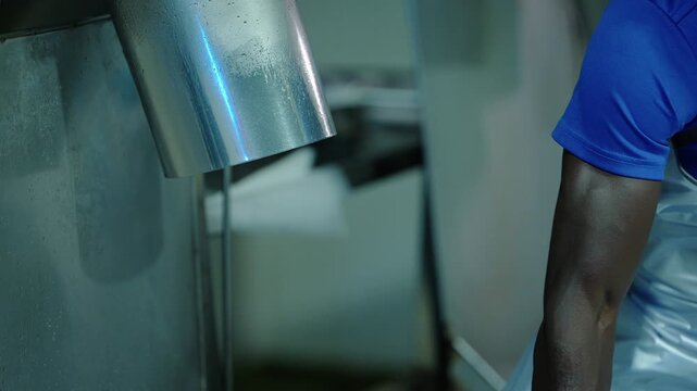 Gloved hand pats a full bag of tube ice then pulls away, leaving the empty stainless chute with water dripping from its outlet in a quiet ice factory in Thailand