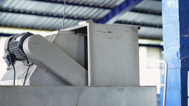 Ice factory worker in a white cap and blue polo leans over a steel ice crusher to feed a block into the machine, then leaves the frame showing the empty crusher