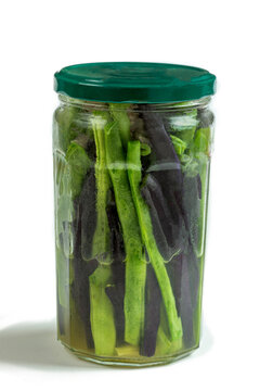 Green and black beans are stored in a glass jar. The jar is sealed with a green lid. The contents are submerged in a clear brine. This is an example of food preservation.