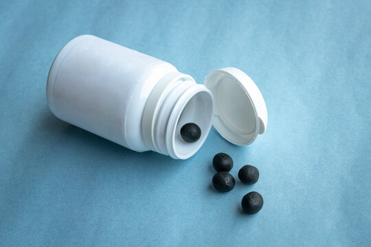 Traditional form of Chinese medicine. Black round pills from a white bottle.