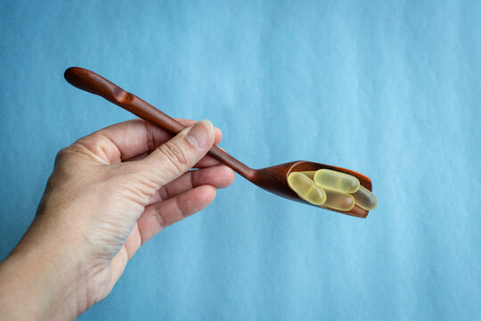 Hand Holding Wooden Spoon With Fish Oil Capsules. Healthcare and medical concept.
