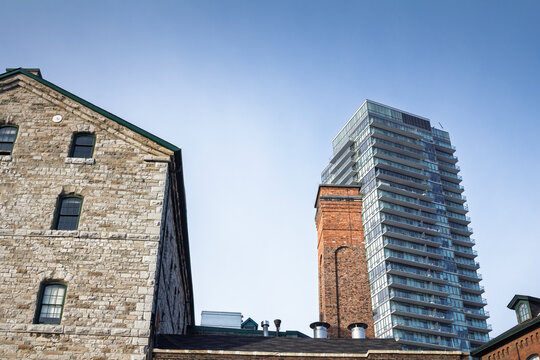 Stone warehouse, old brick chimney and modern glass condo tower in Toronto Distillery Historic District, Canada, showing industrial heritage beside newer residential development and downtown growth.