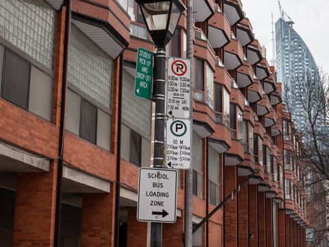 American Parking, student pick-up and school bus loading signs stand beside a red brick Toronto, Canada, showing precise curbside rules and timed restrictions on a North American urban street.