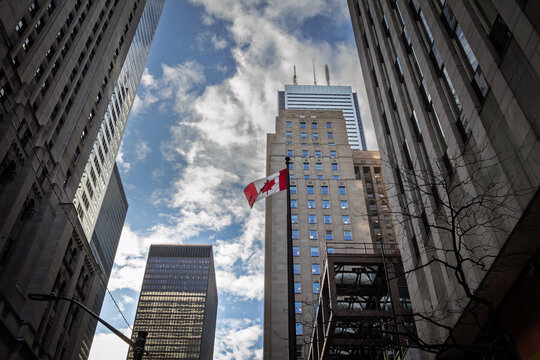 Canadian flag flying among downtown Toronto Canada high rise towers, showing the city business district, finance buildings, modern offices, national symbolism, and urban economy themes.