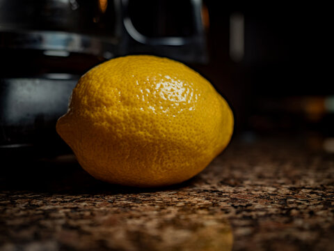Fresh whole yellow lemon sitting on a dark granite kitchen countertop with dramatic moody lighting