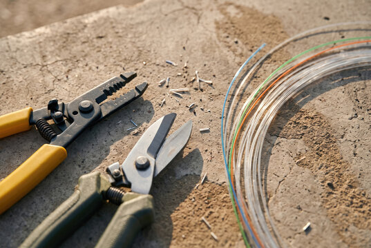 Fiber optic stripper and cable shear beside colorful glass fiber on concrete.