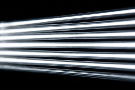 Parallel fiber optic strands glow with white light against dark background, creating sleek abstract pattern with crisp lines and luminous contrast.