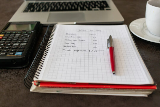 Close-up of finance notebook with pen, calculator, and laptop in background