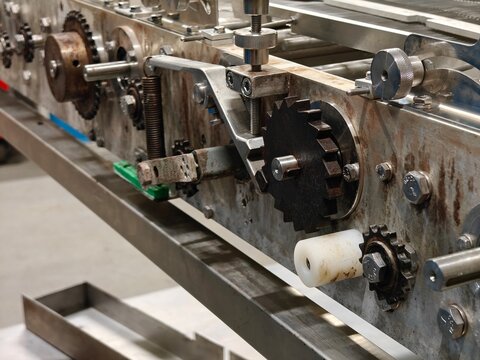 Toothed pulley wheel in a conveyor system with a tension spring.