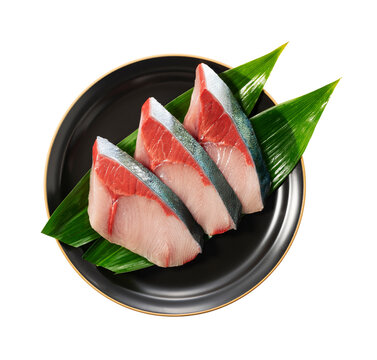 Three raw yellowtail fish fillets on black plate with green leaf isolated on transparent background
