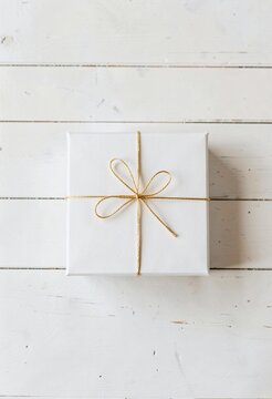 Square white gift box tied with shimmering golden string and bow placed centrally on weathered wooden surface