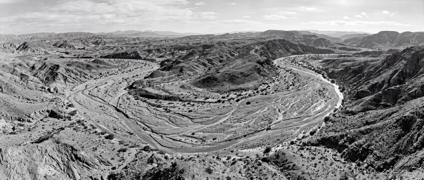 Winding river flowing through vast arid desert mountains under dramatic cloudy sky panoramic landscape