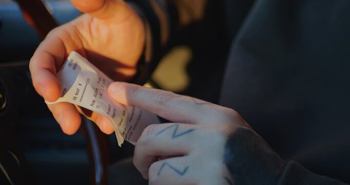 Person holding and examining a fuel receipt at a gas station, checking the total cost and itemized charges. Close-up side view, slow-motion 4K footage about fuel prices and personal finance.