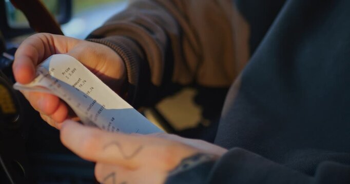 Person examining a printed gas station receipt after purchasing fuel, reviewing the itemized charges, taxes, and final total. Slow-motion 4K footage about rising fuel prices and household expenses.