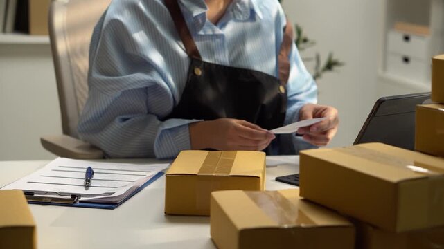 Worker attaches a shipping label to a cardboard parcel for delivery. Close-up ecommerce scene shows order fulfillment, barcode tracking, packing, logistics, shipping preparation, and parcel handling.