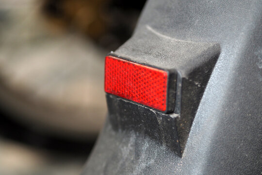 close-up shot of a small red rectangular reflector mounted on a dark, textured plastic surface of a vehicle or equipment.
