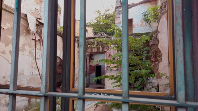 Abandoned historic courtyard with weathered walls, arched doorway, exposed brick and overgrown vegetation surrounding a deteriorating old structure in Cuernavaca Mexico.