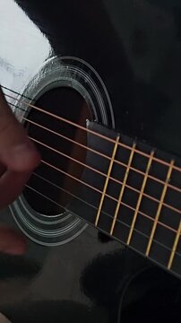 Hands pluck and strum strings on a black acoustic guitar during a close-up performance