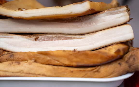 Close-up of stacked slabs of traditional smoked pork lard and bacon fatback displayed on a rustic tray under soft natural daylight for a hearty cuisine concept.