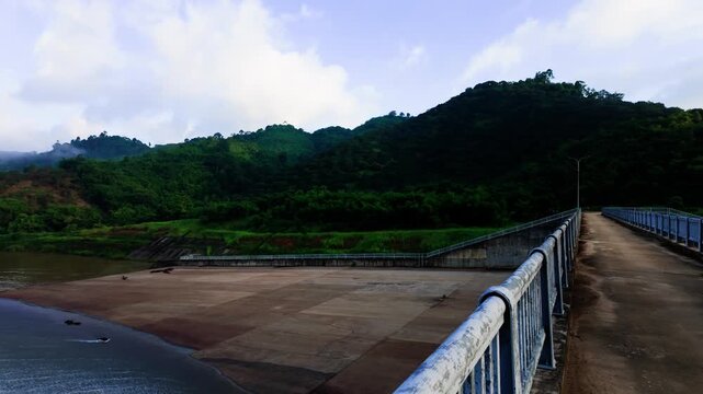 At Da Lay Irrigation Reservoir in Lam Dong, Vietnam, people walk along the dam. Views of the mountains and water provide a backdrop for outdoor activity in the morning sun.