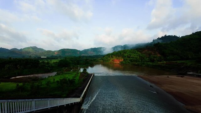 At Da Lay Irrigation Reservoir in Lam Dong, Vietnam, people enjoy the views of the water and surrounding hills. The sun shines bright as clouds drift by, creating a lively atmosphere.