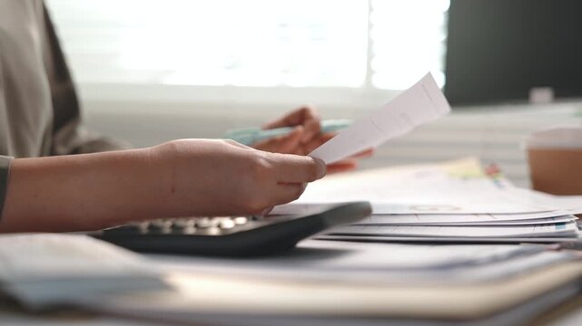Accounting and finance, female accountant sorting financial documents, reviewing paperwork and using calculator at office desk, tax preparation, bookkeeping, audit, budget and year end reporting.