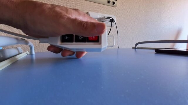 Close-up of a hospital patient pressing the nurse call button beside the bed, requesting medical assistance in a quiet clinical setting.