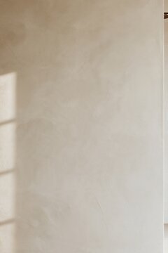 Japandi bathroom wall with warm beige plaster texture and soft sunlight from a nearby window