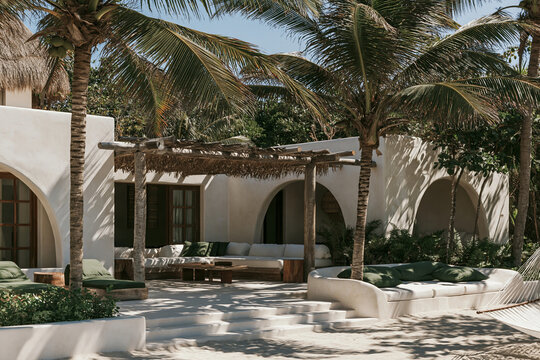 Tropical modern beach club courtyard with palms, white stucco arches, seating, and stone steps