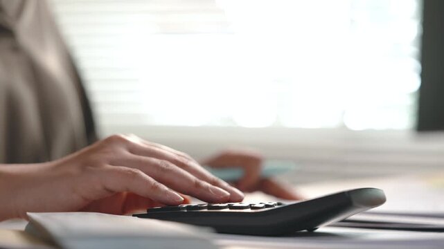 Close up of female accountant using calculator at office desk, calculating financial figures and checking paperwork for accounting, finance, tax preparation, bookkeeping, budget planning and financial