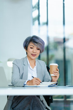 Asian senior businesswoman drinking coffee during work in office