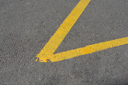 A close up high angle view of yellow painted traffic lines forming a sharp corner on a dark grey asphalt pavement surface.