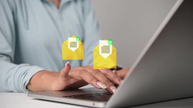 Woman typing on laptop keyboard sending digital newsletter campaign with yellow email envelope icons for online marketing communication in workspace.