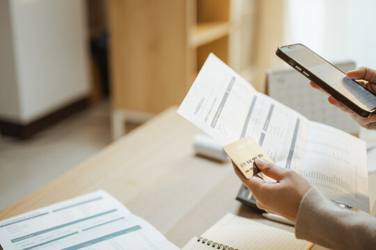 payment comparison planning finance and technology show a person comparing a card, smartphone, and statement, using payment, careful account review, and household budgeting at a home desk.