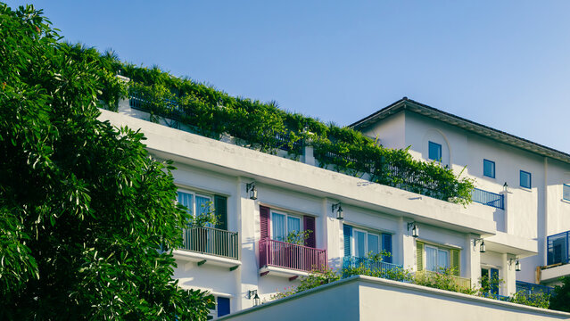 white hotel building featuring colorful balconies plus green roof garden, tropical resort facade with bright shutters lush vegetation under clear blue sky