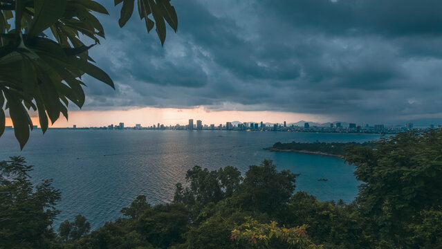 dramatic storm clouds over coastal Da Nang city skyline during sunset over sea, dark tropical weather approaching urban bay featuring panoramic ocean view of Danang