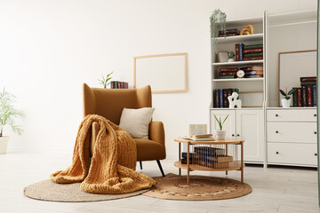 Cozy home interior hygge lifestyle and relaxation with comfortable armchair chunky knit blanket wooden coffee table and bookshelf in room © Pixel-Shot