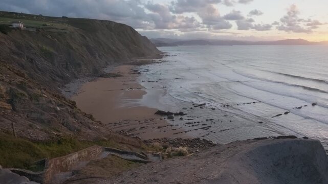 Dramatic ocean view at sunset, capturing waves washing over the unique flysch rock formations along the rugged Bizkaia coastline