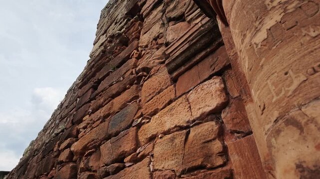 Carved red sandstone wall and fluted column of the San Ignacio Mini Jesuit mission church against cloudy sky, San Ignacio, Misiones, Argentina, low angle tilt up