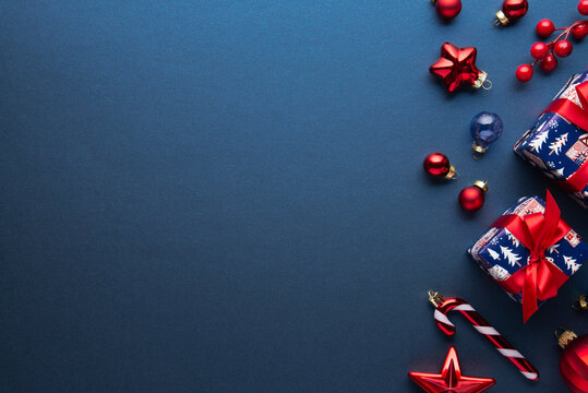 Blue Christmas and Happy New Year holiday background with gift boxes, red ribbon bows and festive red ornaments, flat lay with copy space. Greeting card.