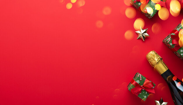Merry Christmas and Happy Holidays greeting card, frame, banner. New Year. Red and golden Christmas ornaments and gifts, presents with champagne on red background top view. Copy space.