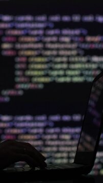 Vertical video. Hacker writing code cracking computer. Programming code in the background. Hacker attack, cybercrime, virus software, dark web, cyber.