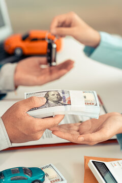 Customer giving stack of dollar banknotes to agent and receiving car key for auto loan or purchase contract