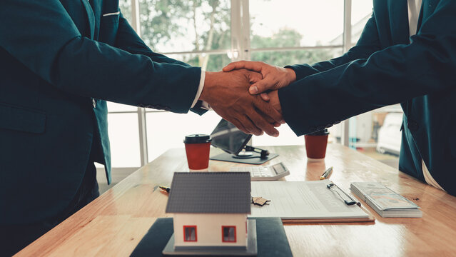 Close up of businessmen shaking hands over a real estate contract deal with house model and keys on desk