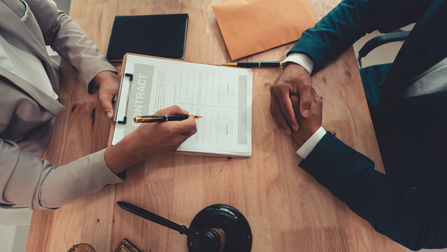Client signing a legal contract agreement document during consultation with lawyer in office