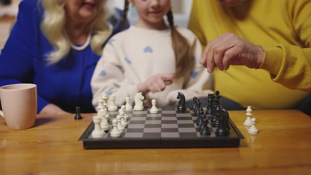 Little girl and grandparents play chess at home, spending quality time together